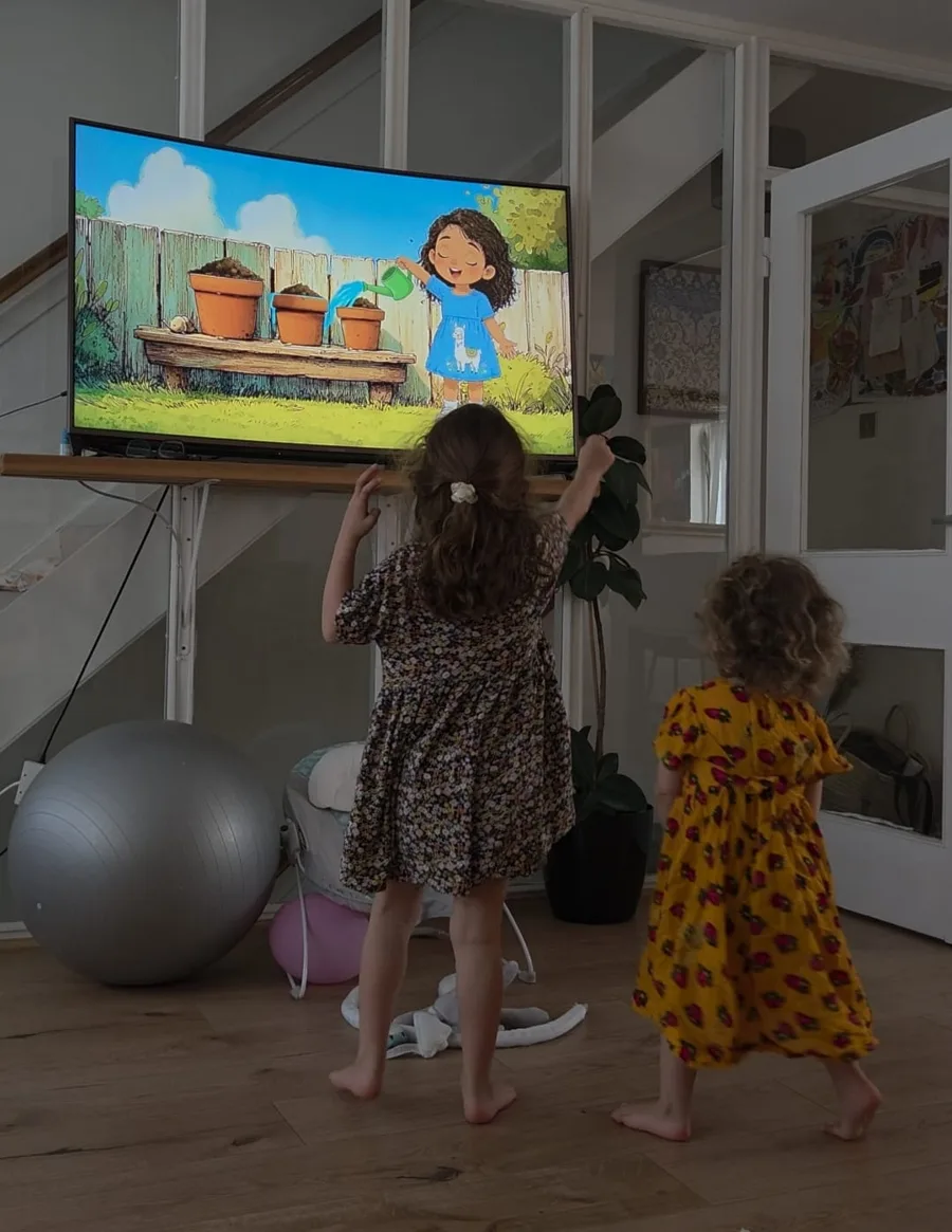 Two young girls dancing in front of a television showing a My Garden Songs animation of Rosy watering terracotta pots